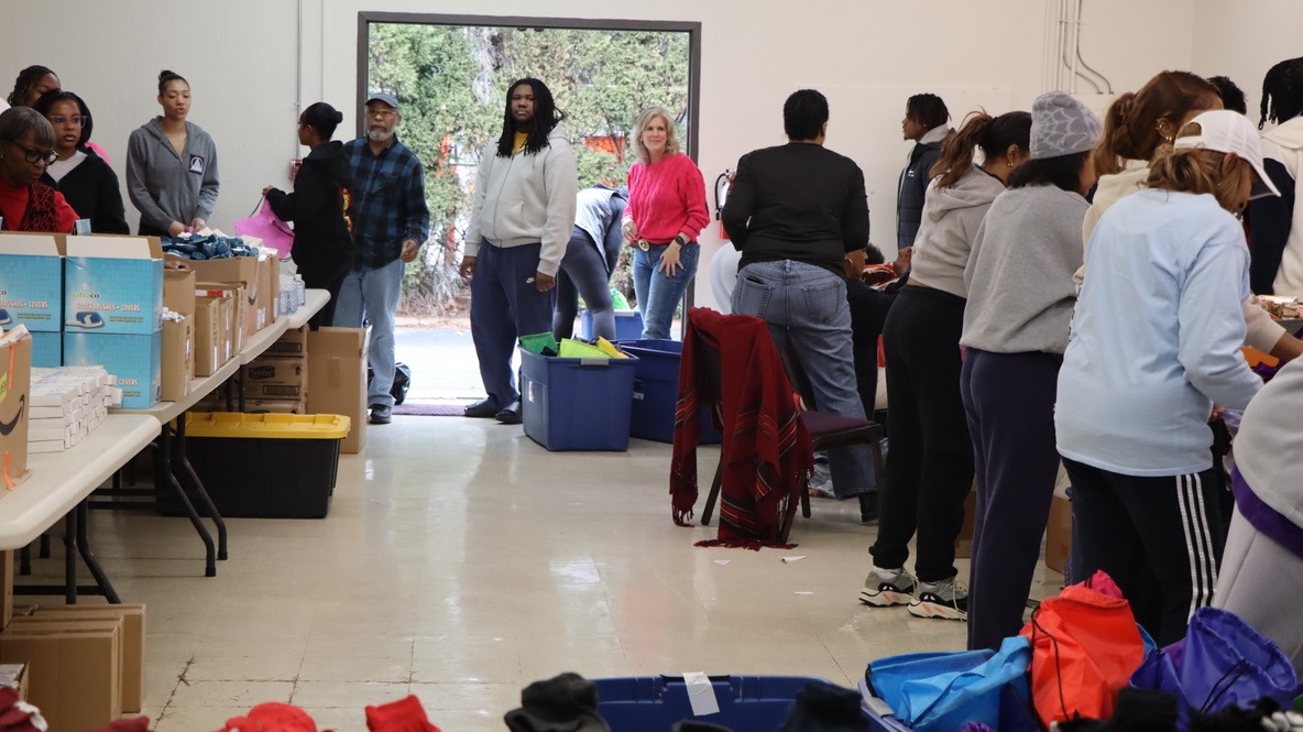 Volunteers sort donations in a large room, with tables filled with boxes and supplies, facilitating community support initiatives.