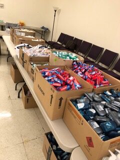 Boxes filled with personal care items like soap and shampoo are neatly arranged on a table in a community space, indicating a distribution event.