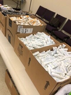 Boxes filled with assorted tubes of cream are arranged on a table, indicating a distribution event for personal care products.