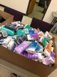 A large box overflowing with various brands and colors of soap bars, illustrating a community donation drive for hygiene supplies.