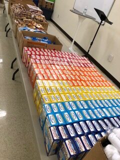 Boxes of brightly colored snacks arranged neatly on a table, with additional containers of cookies in the background, ready for distribution.